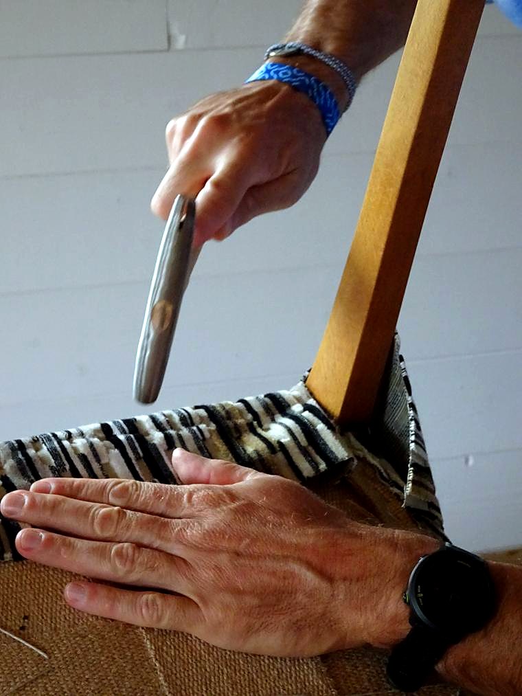 Les mains de Philippe Noret fixant le tissu sur le châssis d'un siège